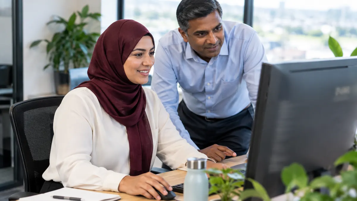 A woman in a headscarf smiling while working with a colleague at a computer in a modern office