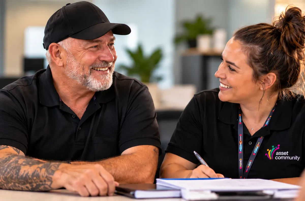 An Asset Community staff member in a branded polo shirt smiling as she talks with a participant at a desk
